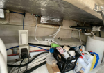 Cluttered utility area under a ceiling, with exposed pipes, cables, and a crate of cleaning supplies.