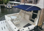 Open rear deck of a white motor yacht with a blue canopy, small table and captain-style chairs, docked at a marina