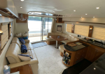 Luxurious yacht salon with beige leather seating, oval wood table, and built-in kitchenette, facing deck doors.