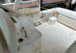 Cream-colored boat cockpit with cushioned seats, cockpit console, and a yellow power cord along the railing near a small cooler.