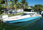 Blue and white motor yacht docked in a calm canal beside a palm-lined backyard with a pool area visible behind it.