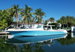 A white and blue motorboat docked in calm canal with palm trees and a white house in the background under a clear blue sky.