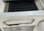 Open grill compartment with a black metal grate, set in a white kitchen cabinet with a chrome handle above the drawer area.