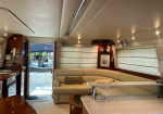 Interior of a luxury yacht living area with a cream L-shaped sofa, wood cabinetry, and a door to the deck outside the cabin.