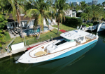 A white luxury motor yacht docked in a canal beside a tropical backyard with a pool and palm trees at a modern home.