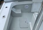 White boat cockpit/deck area with built-in seating, round deck hatches, and a speaker on the gray wall panel near lockers.