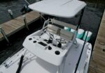 White center-console boat docked at a wooden pier, with two beige captain seats and a steering wheel at the helm.