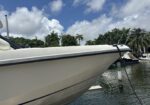Close-up of a white boat bow docked at a marina with water, palm trees, and blue sky in the background