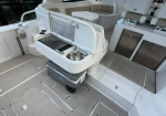 White boat deck with built-in grill and cooler, seating area in the background near a marina.