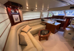 Luxurious yacht salon: curved cream leather sofa, throw pillows, wood paneling, and a glass coffee table near a built-in galley.