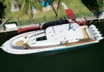 Aerial view of a white luxury yacht docked at a marina, with palm trees nearby and a red dock in the background.
