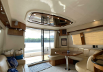Luxurious yacht salon with cream leather seating, a round wooden table, and large windows showing water outside, natural light filling the space