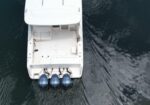 Top-down view of a white boat from above, showing four blue outboard motors at the stern in dark water