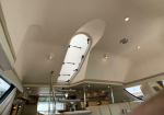 Luxurious yacht interior with a curved white ceiling, oval skylight hatch, and a staircase leading to the upper deck.