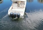 Top-down view of a white motorboat on blue water, showing seating area and three outboard engines at the stern