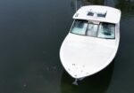 A white motorboat viewed from above on dark water, bow toward the bottom right with a windshield and navigation equipment on the cabin roof