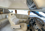 Luxurious beige boat cockpit with a plush captain's chair, curved beige seating, and large windows surrounding the helm.