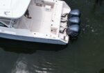 Top-down view of a white motorboat docked in dark water, showing three Yamaha outboard engines at the stern and a small person standing on the deck near the cabin.