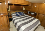Wood-paneled boat cabin with a queen bed, gray-and-white striped quilt, navy starfish pillows, and built-in cabinets along the sides.