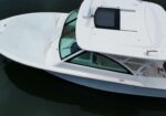 Aerial view of a white motorboat docked on dark water, with a canvas cover over the bow and a man standing on the rear deck.