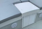 White built-in storage cabinet between gray cushioned boat seats; round marine speakers on the sides and vented doors on the cabinet visible.