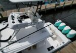 White sportfishing boat cockpit with helm, steering wheel, gauges, and rod holders docked at a wooden marina docked by calm water.