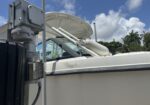 Close-up of a white boat tied to a dock with a metal post and rope fender in the foreground, boat cabin and windshield visible under a blue sky.