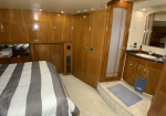 Wood-paneled yacht cabin with a striped bed, built-in cabinets, and a small ensuite vanity area to the right.