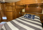 Wood-paneled bedroom cabin with built-in storage, a large bed in the center, and a striped gray-and-white quilt plus blue nautical pillows