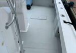 White boat cockpit deck with stainless railing, a rectangular deck hatch in the center, and rigging along the gunwale.