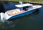 White and blue luxury motor yacht cruising on dark water, with a wide open aft deck and multiple outboard engines at the stern.