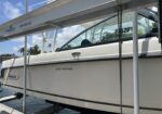 White Boston Whaler 270 Vantage boat on a lift at a marina, with blue sky and palm trees in the background. The hull shows the name 270 Vantage and Boston Whaler branding.
