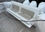 White boat cockpit with a fold-down bench seat and beige patterned cushions; outboard engines visible in the background