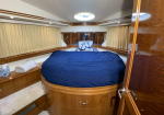 Round bed with navy comforter and an anchor-pattern pillow in a wood-paneled yacht cabin, beige curtains along the sides, porthole window above.