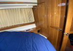Interior cabin with a blue quilted bed, wooden built-in cabinets, and cream curtains along the wall.