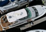 Top-down view of white luxury motor yachts docked at a marina, with wooden aft decks and blue canvas covers visible on one boat.