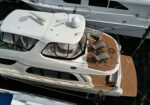 Aerial view of a white yacht with wooden aft deck and two gray lounge chairs on the stern, docked beside another boat.