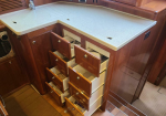 Wood-paneled yacht galley with many small drawers open under a light countertop, exposing contents.