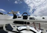 Close-up of a boat helm with a chrome steering wheel and black control console on a white yacht deck under a blue sky
