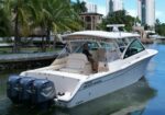White Grady-White powerboat docked in a canal with palm trees and high-rise buildings in the background.