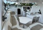 White boat cockpit with curved beige-cushioned seating around a small table and twin captain chairs at the helm.