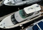 Aerial view of white luxury yachts docked side by side at a marina, wooden deck, and dark water below.