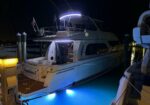 Luxury motor yacht moored at a marina at night with blue underwater lights illuminating the water near the stern.