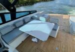 Luxurious yacht aft deck with white cushioned seating, light blue pillows, and a white rectangular table on a teak deck by blue water.