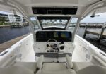 White luxury boat cockpit facing forward, with dual navigation screens and a chrome steering wheel, dock and calm water visible outside.