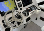 Boat helm with steering wheel and multiple navigation screens displaying map and engine data (marine cockpit).