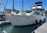 White motor yacht docked at a marina under a clear blue sky, with a flybridge and deck fittings visible.