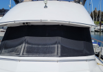 Front view of a white motor yacht with a black cockpit cover and clear windows, moored at a marina under a bright blue sky.