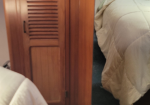 Wooden cabin interior featuring a louvered cabinet door and a bed along a wall with beige bedding.