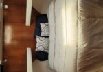 A neatly made bed with white quilt and decorative pillows against a wooden paneled wall in a small cabin.